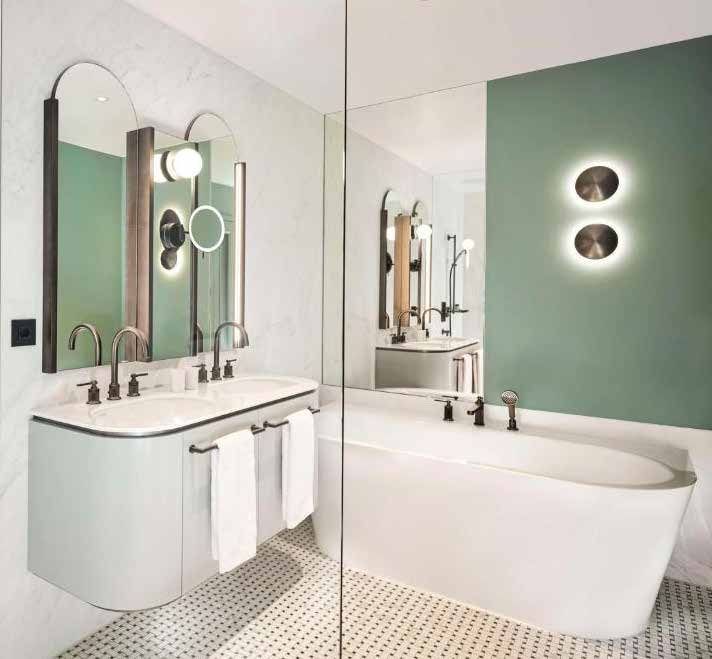 Bad eines Zimmers: weißer Doppelwaschtisch mit Rundbogenspiegeln, Badewanne hinter einer Glaswand, mintgrüne Wand mit zwei runden Wandleuchten