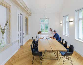 Besprechungsraum mit langem Holztisch und schwarzen Stühlen, hohe Sprossenfenster und freigelegte Sandsteingewände