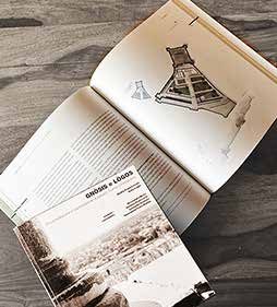Die gedruckte Masterarbeit „Gnòsis e Lògos“ aufgeschlagen auf einem Holztisch: Doppelseite mit Axonometrie der Festung, darunter der Umschlag mit historischem Foto