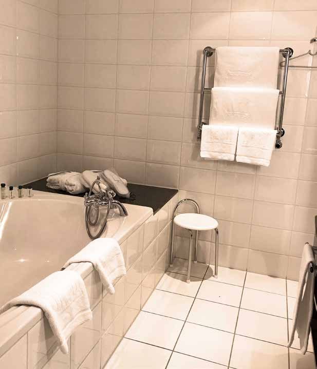 Das Bad der Hochzeitssuite vor der Sanierung: weiß geflieste Wände, eingebaute Badewanne und Handtuchheizkörper