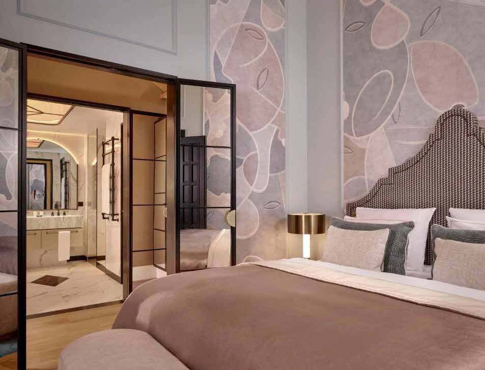 Die Hochzeitssuite heute: Bett mit hohem Kopfteil vor rosa Bildtapete, Blick durch schwarz gerahmte Glastüren ins Bad