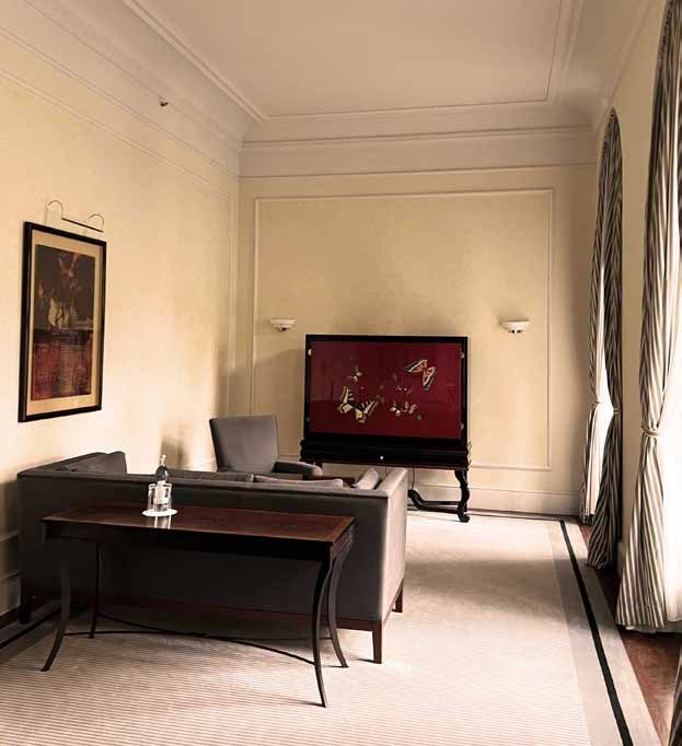 Das Wohnzimmer der Hochzeitssuite vor der Sanierung: beige Wände, Schreibtisch, dunkles Sofa und roter Lackschrank