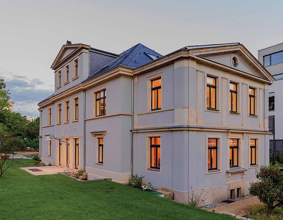 Nachher: Eckansicht der sanierten Villa in der Abenddämmerung, erleuchtete Fenster, neues Schieferdach, gepflegter Rasen
