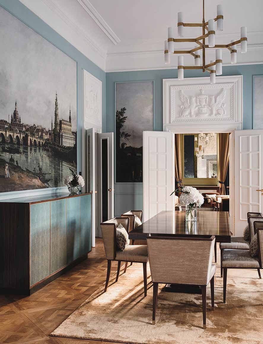 Das Wohnzimmer des Königs heute: hellblaue Wände mit historischer Dresden-Ansicht als Wandbild, Stuckrelief über der Tür, Esstisch mit Stühlen und Messingleuchter